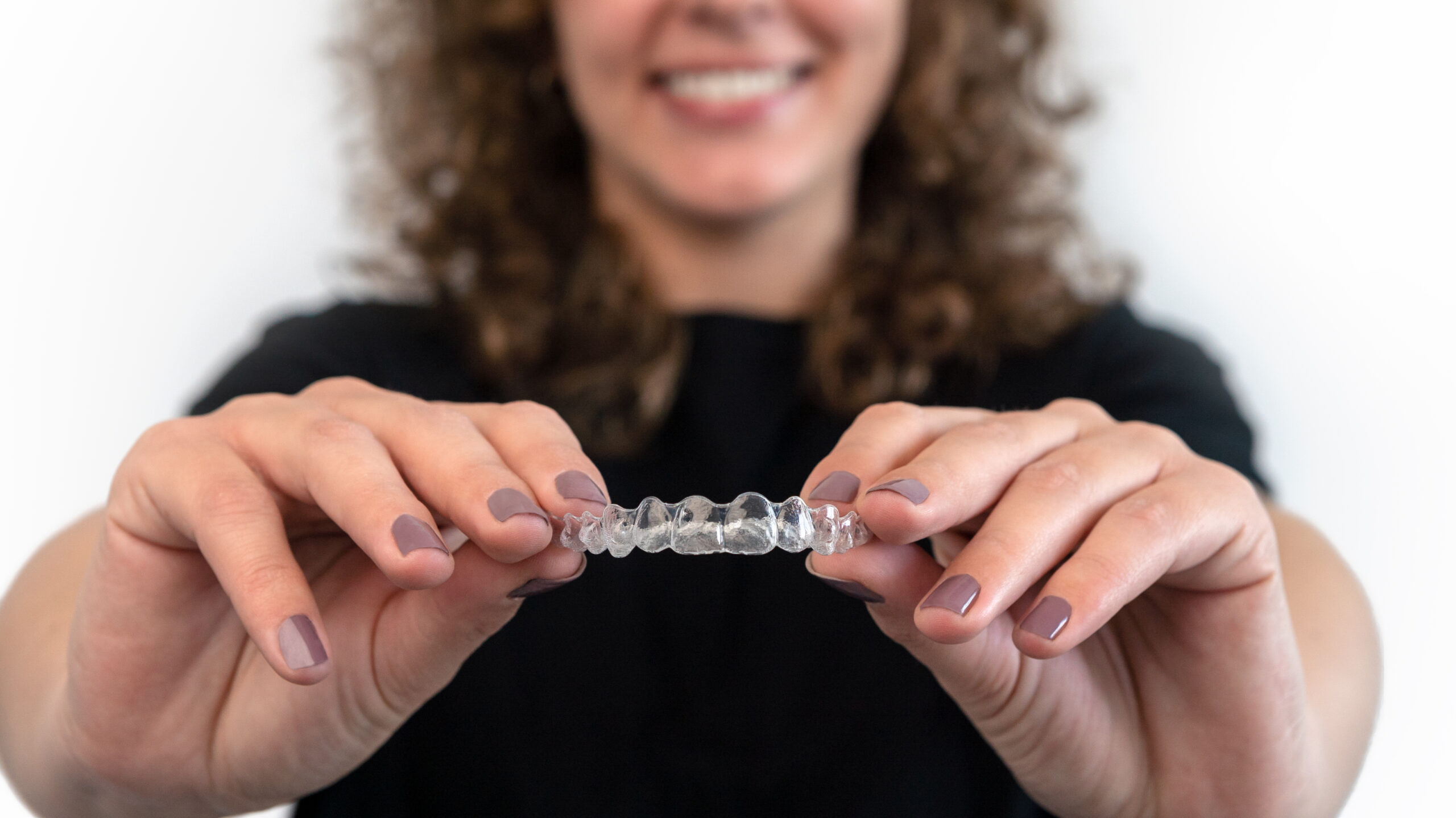 Caucasian young woman showing an invisible silicone aligner for dental correction. Female hand holding the plastic braces dentistry retainers to straighten teeth